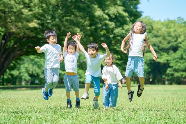 野原で元気いっぱいジャンプする5人の子ども